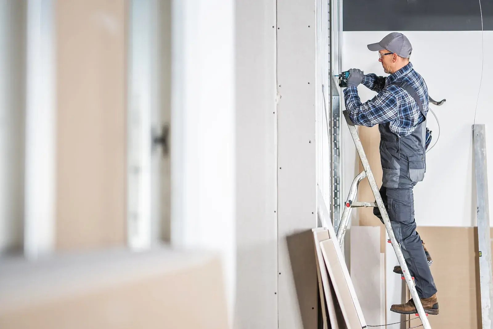 Vakman monteert vanaf een ladder een metal stud wand tegen het plafond.
