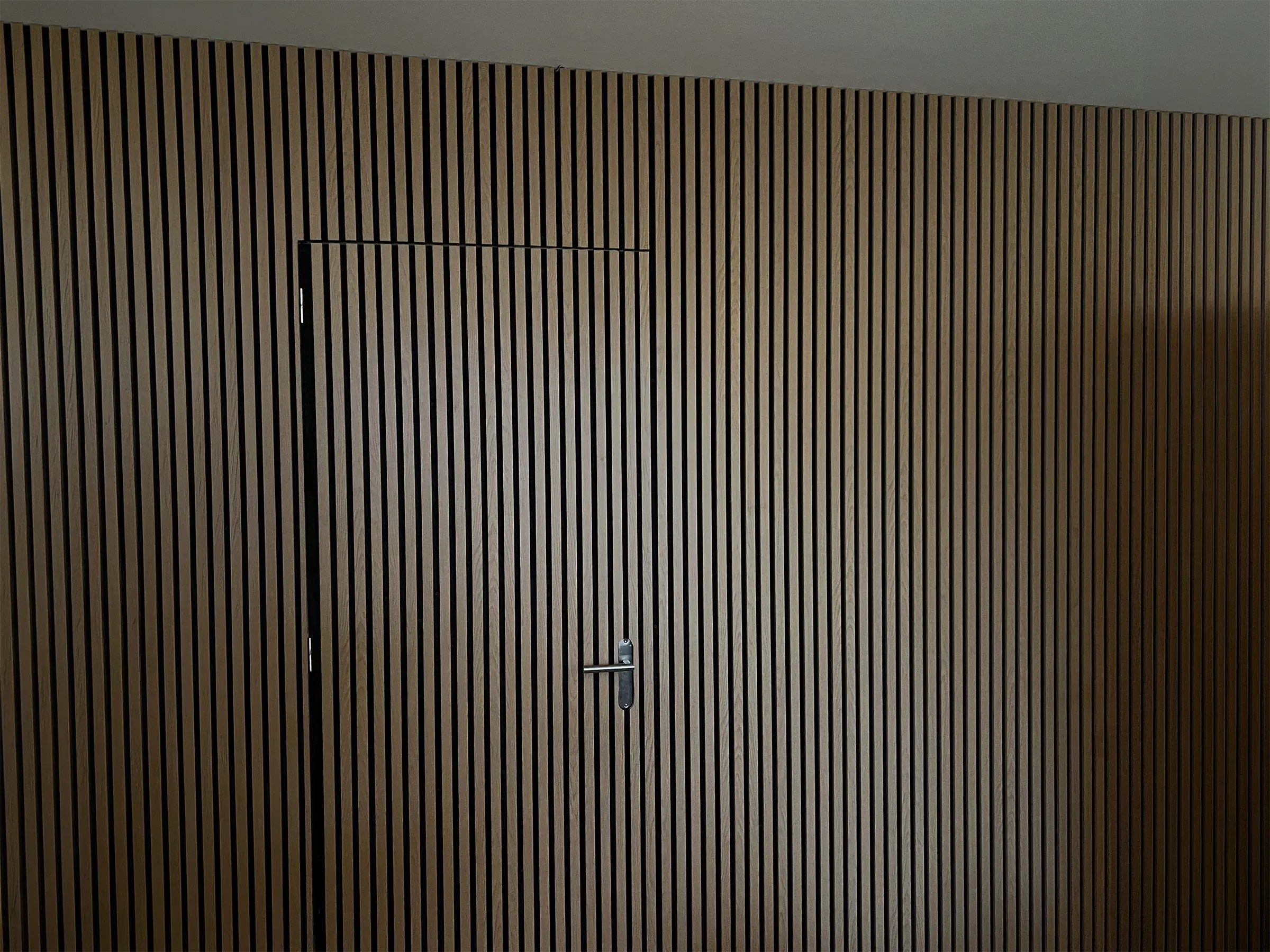 Tussenwand met eiken akoestische lamellen, met een deur naar de nieuwe slaapkamer die met dezelfde lamellen is bekleed.